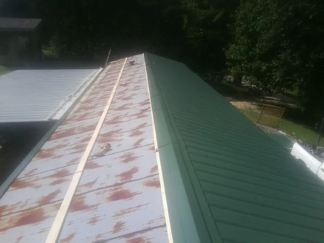 Old rusted panels beside newly installed green metal roofing — Wind Damage Roof Repair by Roofing Brothers in Genoa