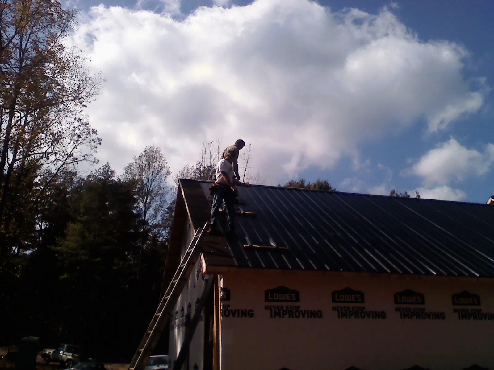 Roofer fastening dark metal panels high against a cloudy sky, from a Roof Inspection job in Genoa