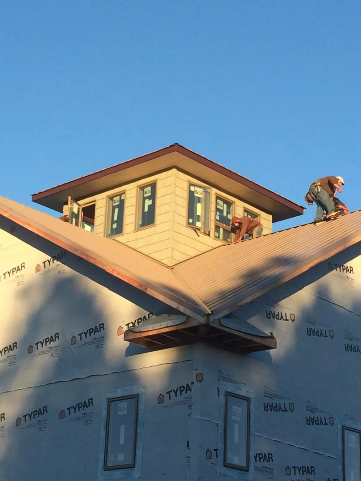 Roofers working around a rooftop cupola on a new metal roof at sunset — Roof Waterproofing in Genoa by Roofing Brothers